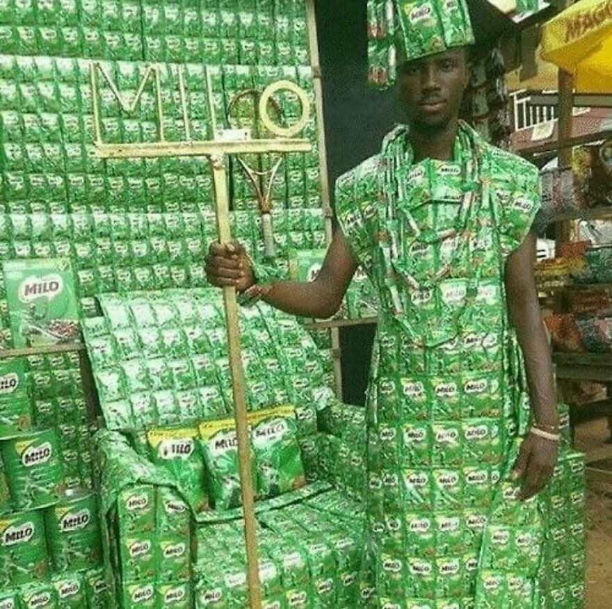 A man dressed in an outfit made of Milo packets, holding a staff, surrounded by Milo packaging, a cursed image.