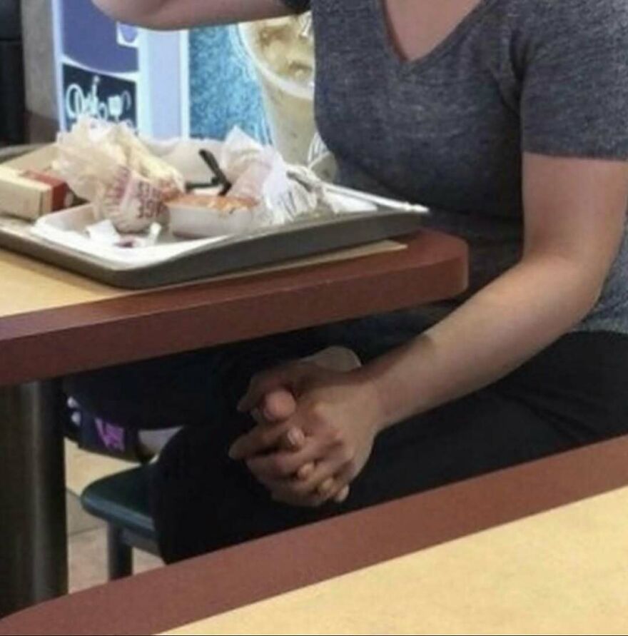 A person with an extra pair of hands folded together at a table, a random and unhinged image.