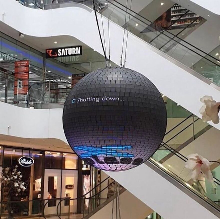 A large disco ball hanging in a mall, displaying a shutdown message, presenting a cursed and unhinged scene.