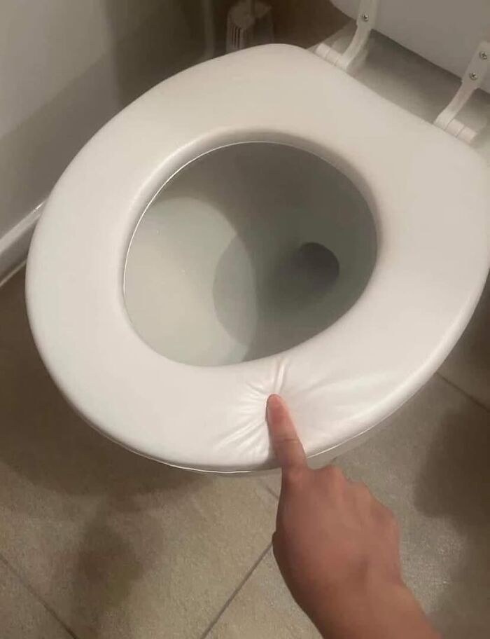 A finger poking a soft, squishy toilet seat cover, a common item that brings '90s and '00s nostalgia.