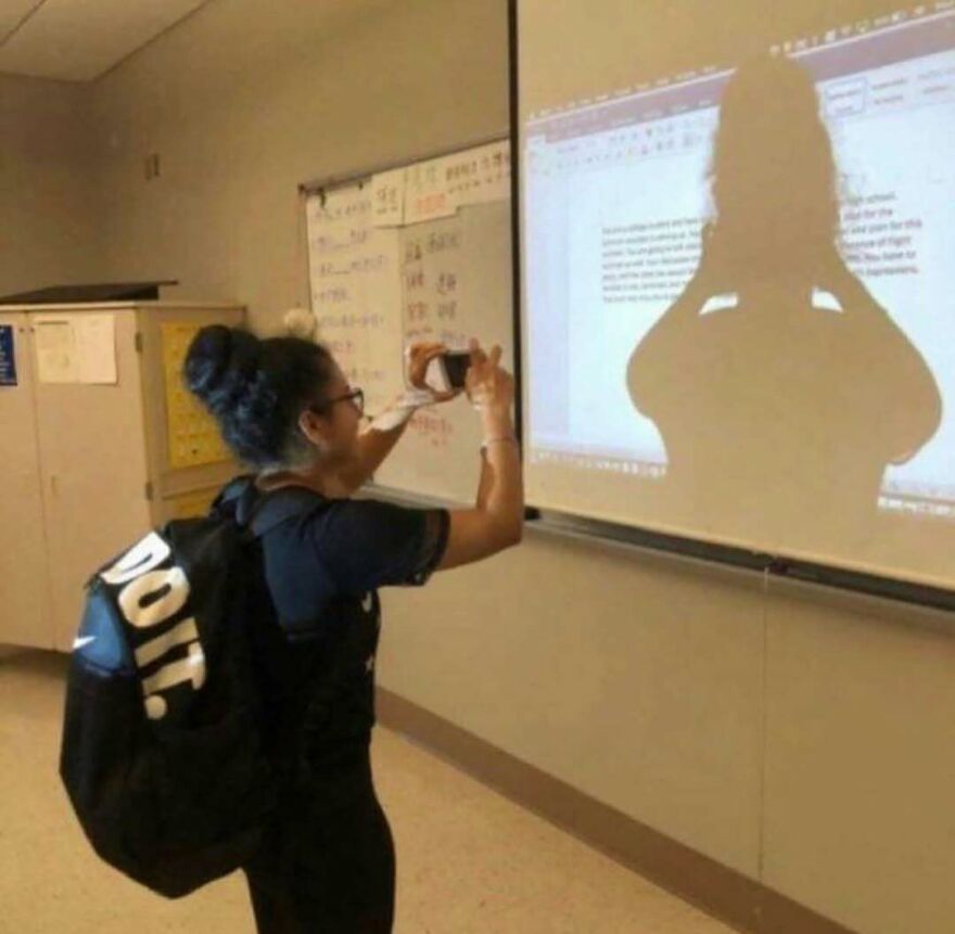 A girl taking a picture of her own silhouette on a projector screen, an unhinged image.