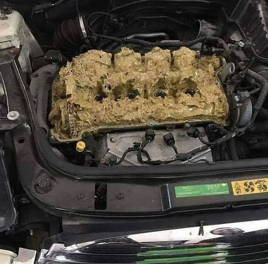A cursed image of a car engine caked in thick, yellow, unhinged sludge, looking very random and unclean.