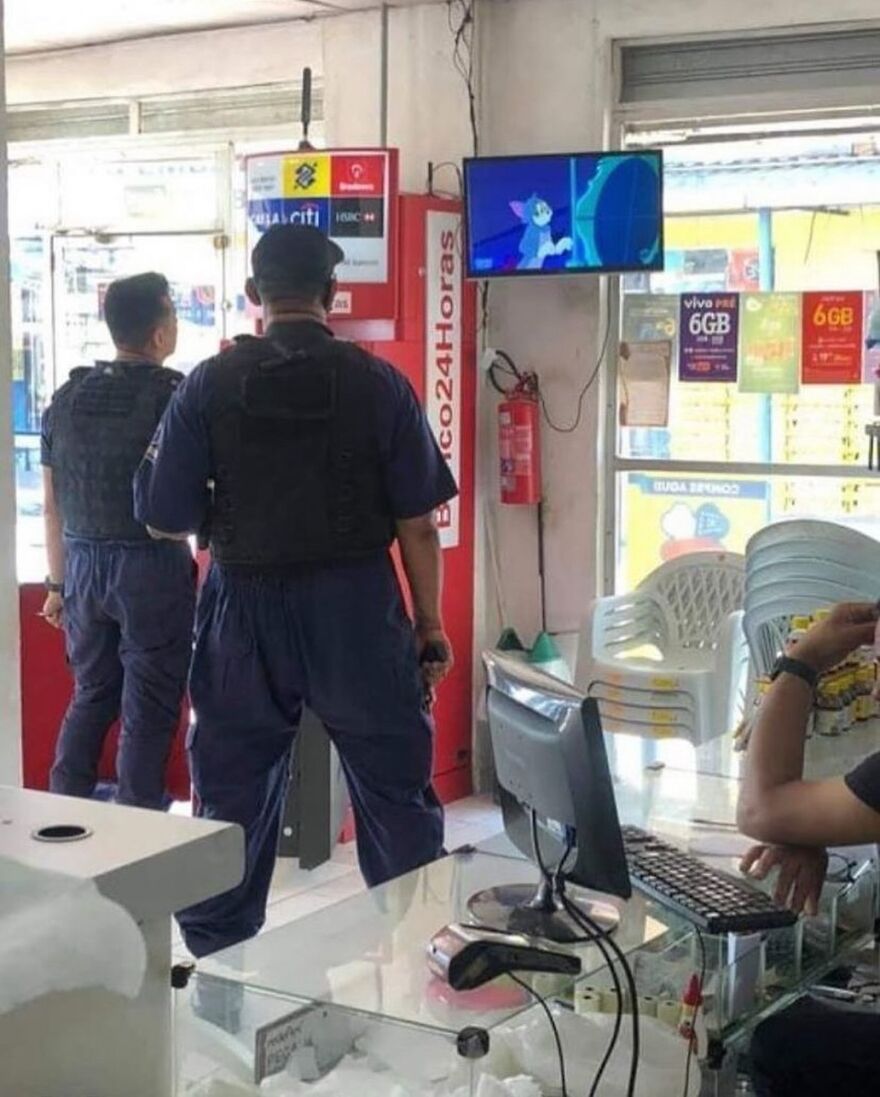 Two security guards in uniform standing in a store while Tom and Jerry cartoon plays on a TV, an unhinged image.