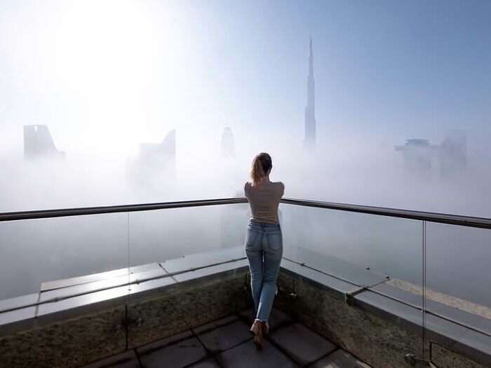 A woman on a rooftop overlooking a foggy cityscape, a remarkable photograph capturing landscapes by Tittu Shaji Thomas.