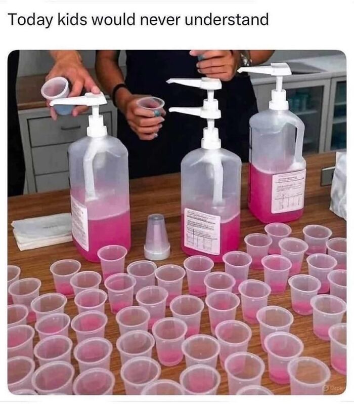 A photo of three large pink liquid dispensers and many small plastic cups, evoking Saturday mornings nostalgia.