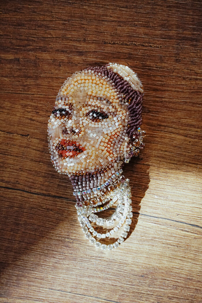 A captivating beaded creation by Tiffany Pisani depicting a woman's face with a pearl necklace, resting on a wooden surface.