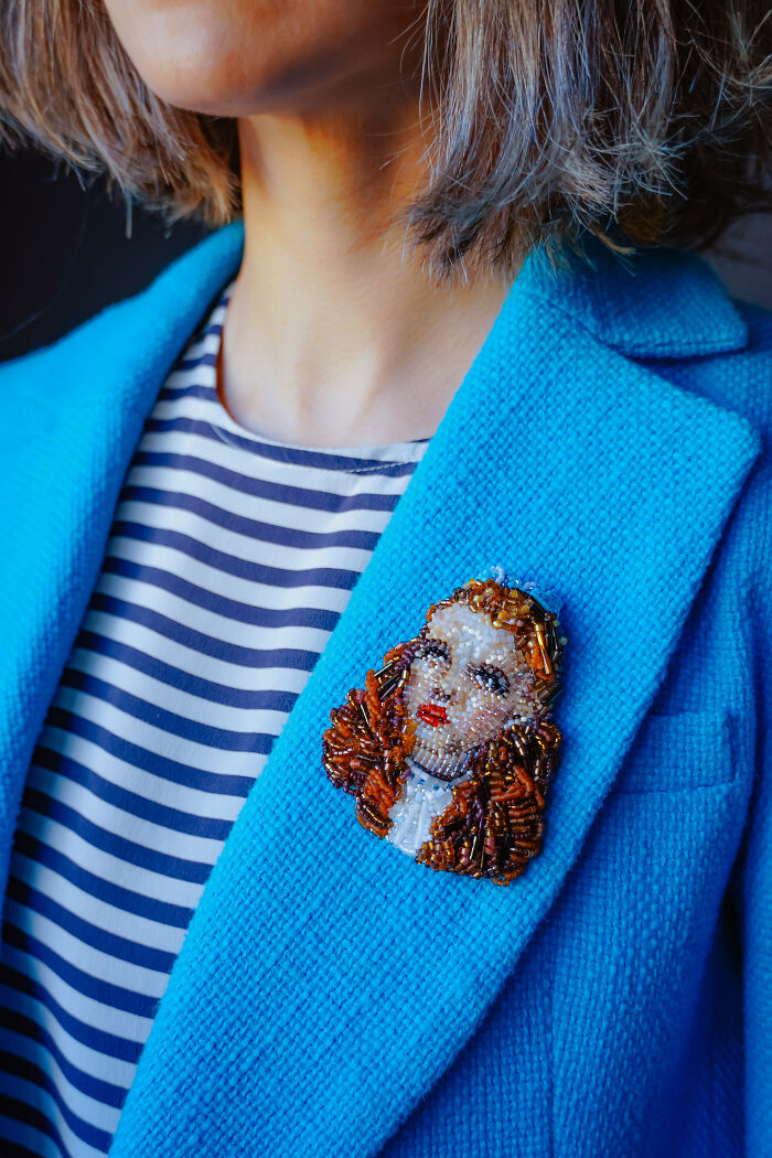 A woman wearing a vibrant blue jacket featuring a beaded creation brooch by Tiffany Pisani.
