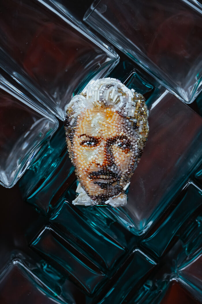 Beaded creation by Tiffany Pisani, a detailed male portrait brooch, resting on a collection of glass bottles.