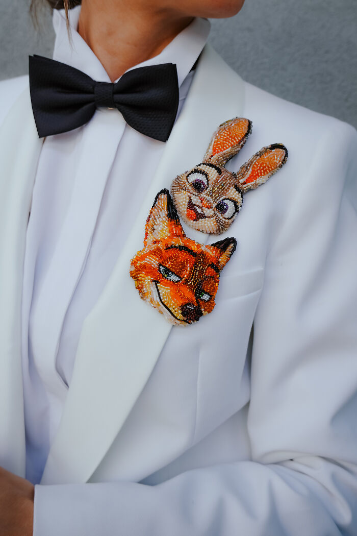 Two cartoon character brooches, a bunny and a fox, by Tiffany Pisani, adorning the lapel of a white tuxedo jacket with a black bow tie.
