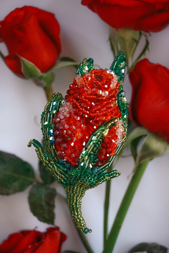 An exquisite beaded creation by Tiffany Pisani, a vibrant red rose brooch, nestled among fresh red roses.