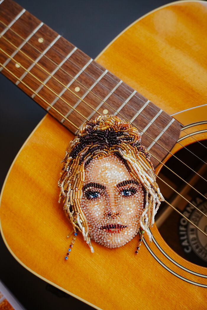 A detailed beaded creation by Tiffany Pisani, depicting a woman's face, resting on the body of an acoustic guitar.