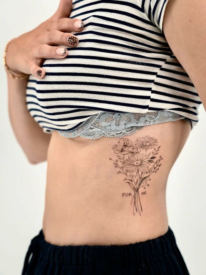Floral rib tattoo ideas for women, featuring a delicate bouquet of daisies and other flowers, making a subtle design.