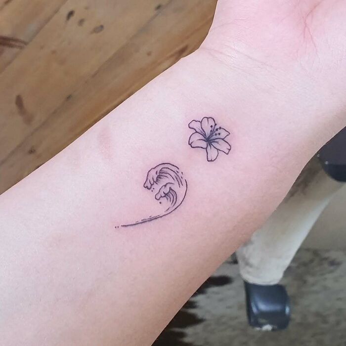 A small semicolon tattoo with a wave and a flower, symbolizing a powerful story on the wrist.