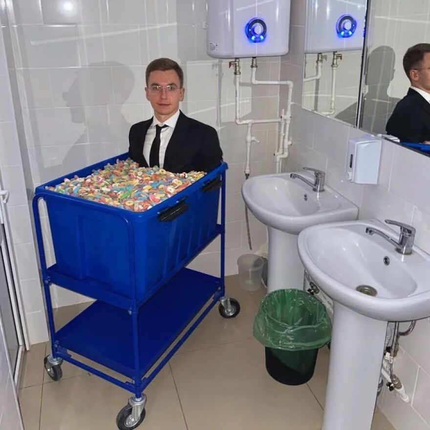 A man in a suit in a blue cart filled with candy in a restroom, an unhinged and cursed image.