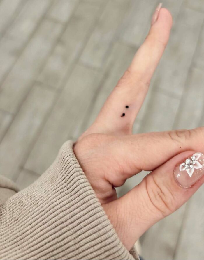 A tiny semicolon tattoo on a finger, a small symbol with a powerful story of strength and continuation.