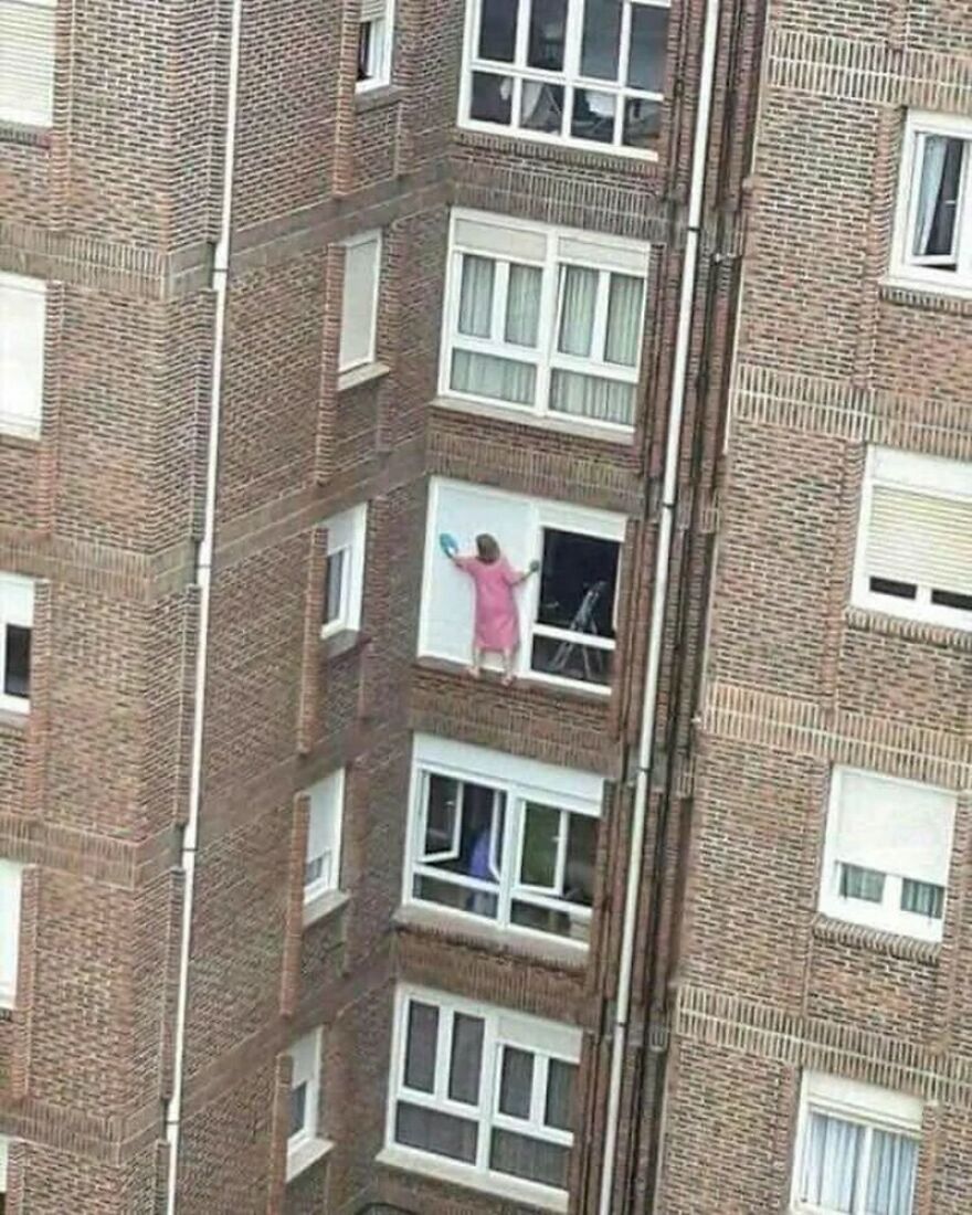 A person in a pink robe cleaning a window from the outside of a high-rise building, an unhinged image.