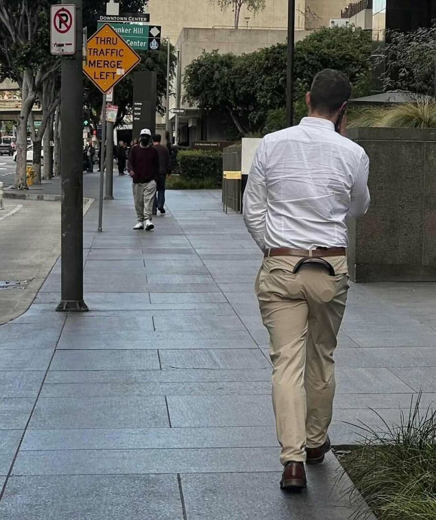 A man walking down a city street with something peculiar hanging from his belt, one of the cursed images.