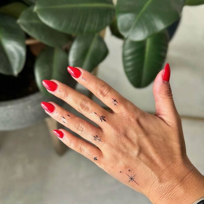 Tiny finger tattoo ideas for women, minimalist designs on a hand with red nails.