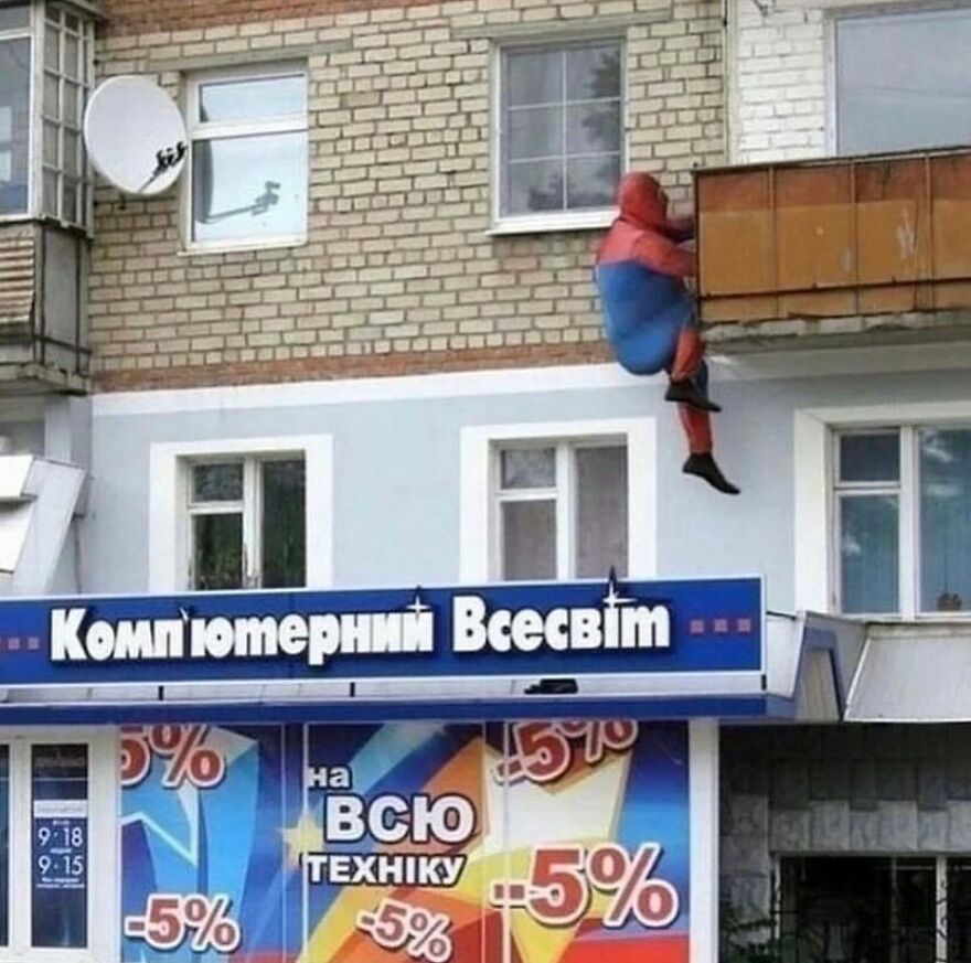A person in a Spider-Man costume clinging to a building balcony, a random and unhinged image.