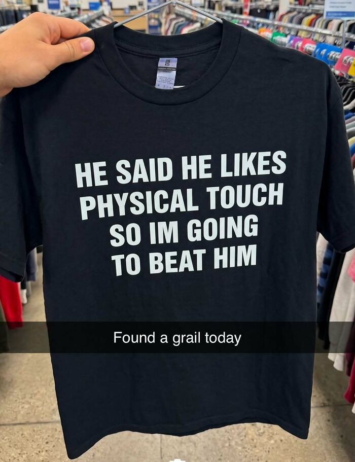 A hand holding up an iconic black shirt with the phrase: HE SAID HE LIKES PHYSICAL TOUCH SO IM GOING TO BEAT HIM.