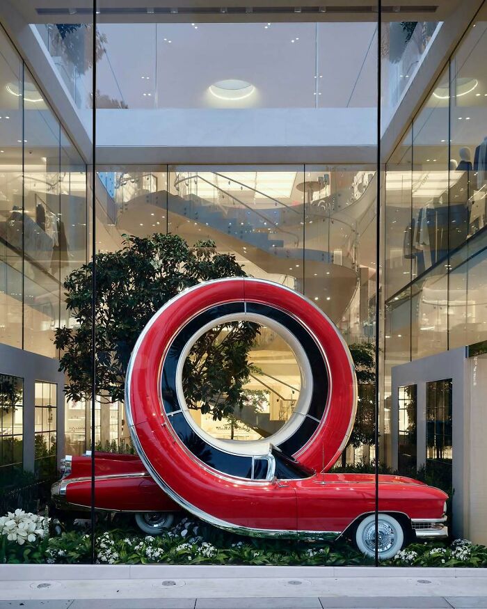 A vintage red car with an oversized, stylized spare tire displayed as a brilliant design in a modern glass building.