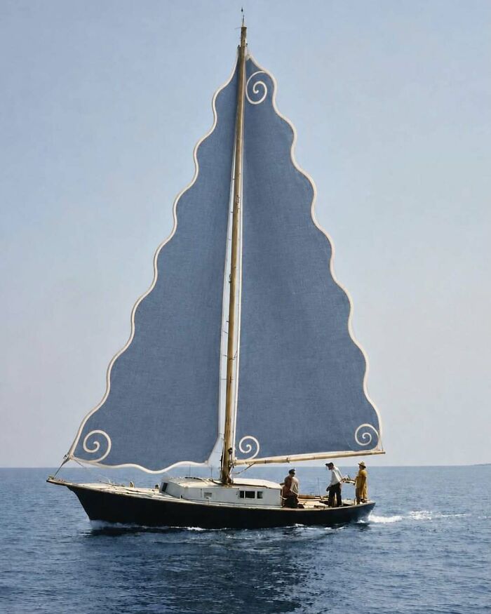 A classic sailboat with a distinctive wavy blue sail adorned with white spirals, a brilliant and beautiful design.