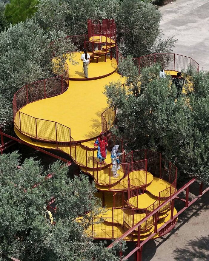 An aerial view of a unique winding yellow walkway with red railings through lush trees, showcasing brilliant designs.
