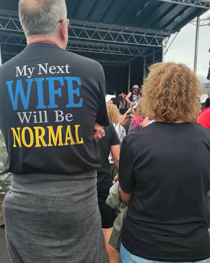 Iconic shirts, a man wearing a black shirt that reads 'My next wife will be NORMAL' at a public event.