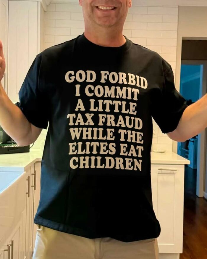 A man wearing an iconic black shirt with the text: GOD FORBID I COMMIT A LITTLE TAX FRAUD WHILE THE ELITES EAT CHILDREN.