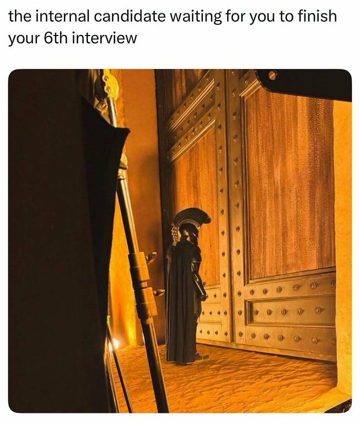 Pop culture post: A person in a black costume stands before a large golden door, like an internal candidate waiting for an interview, for good vibes.