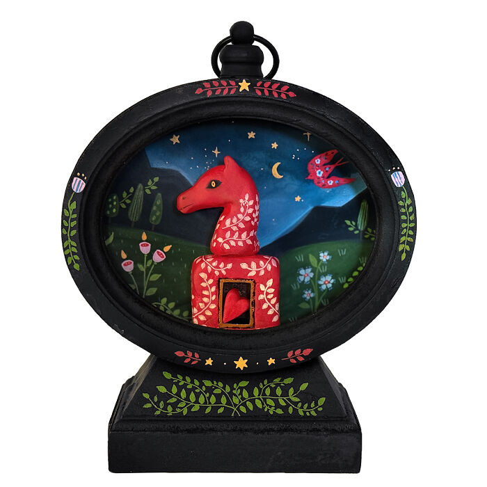 Folk-inspired artwork by Aunia Kahn: a red horse head sculpture with a heart, set in an imaginative nocturnal landscape with a bird.