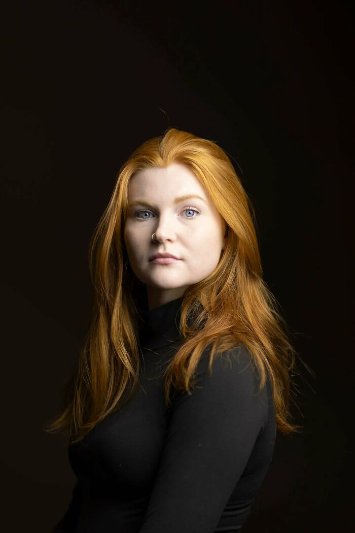 A striking natural redhead woman with blue eyes and a black turtleneck, from a global portrait project.