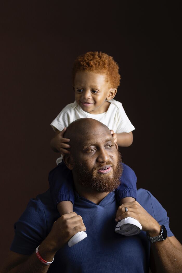 A natural redhead child with curly hair sitting on a man's shoulders, from a global portrait project.