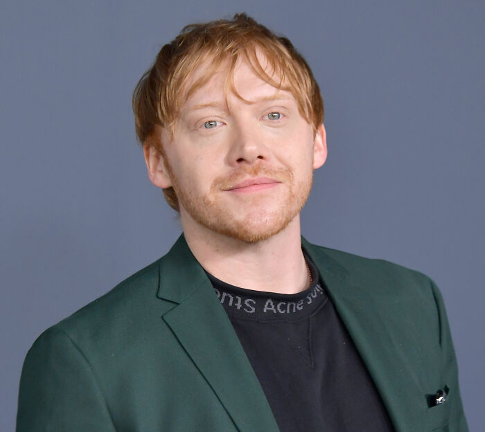Rupert Grint in a green blazer, looking at the camera, after announcing return to his Harry Potter role. Rupert Grint in a green blazer, looking at the camera, after announcing return to his Harry Potter role.