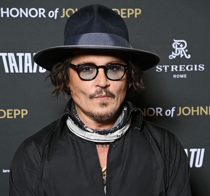 Johnny Depp looking at the camera, dressed in a black shirt and hat, at an event, relevant to his Hollywood star status. Johnny Depp looking at the camera, dressed in a black shirt and hat, at an event, relevant to his Hollywood star status.