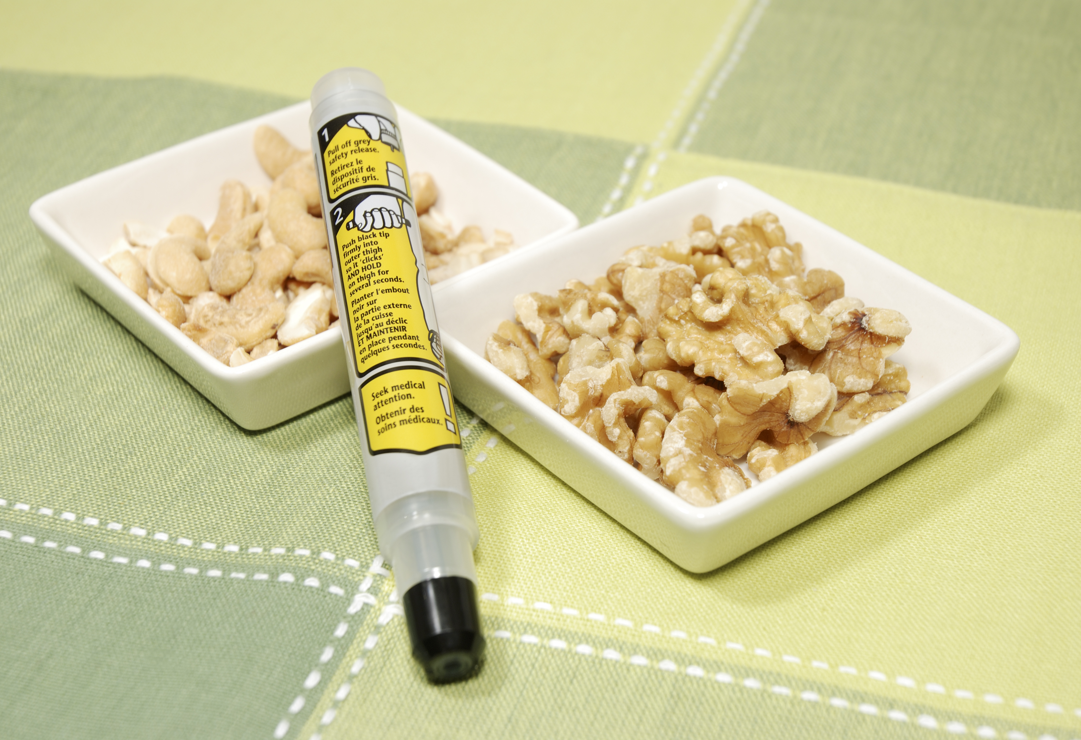 An EpiPen device next to small white dishes of cashews and walnuts for a woman's boyfriend forgetting her allergy. An EpiPen device next to small white dishes of cashews and walnuts for a woman's boyfriend forgetting her allergy.