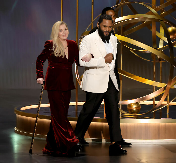 Christina Applegate, using a cane and assisted by Anthony Anderson, on stage, addressing her health battle. Christina Applegate, using a cane and assisted by Anthony Anderson, on stage, addressing her health battle.