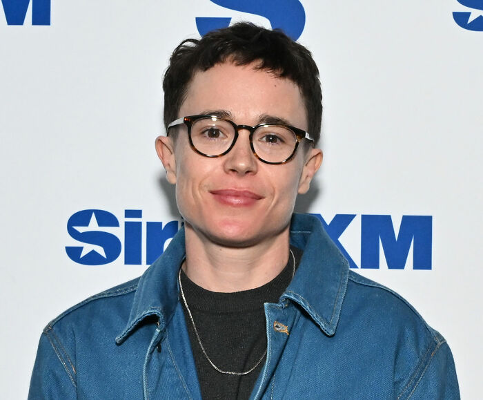 Elliot Page in glasses, standing against a white backdrop with blue SiriusXM logos, discussing queer and trans people.