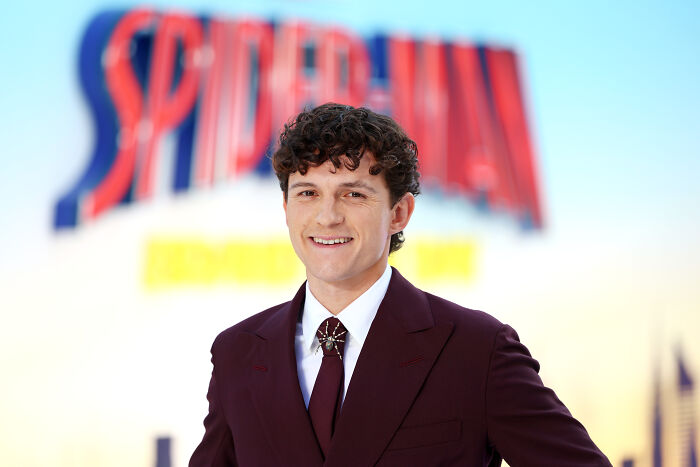 Tom Holland smiling in front of a Spider-Man logo, emphasizing his role among great actors. Tom Holland smiling in front of a Spider-Man logo, emphasizing his role among great actors.
