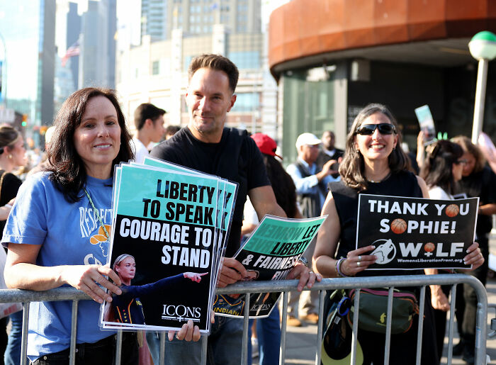 Anti-Trans Protesters hold signs supporting liberty to speak and women's liberation at a WNBA game. Anti-Trans Protesters hold signs supporting liberty to speak and women's liberation at a WNBA game.