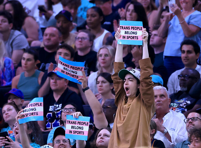 Fans in the crowd at a WNBA game hold signs saying Trans People Belong in Sports, supporting trans athletes. Fans in the crowd at a WNBA game hold signs saying Trans People Belong in Sports, supporting trans athletes.
