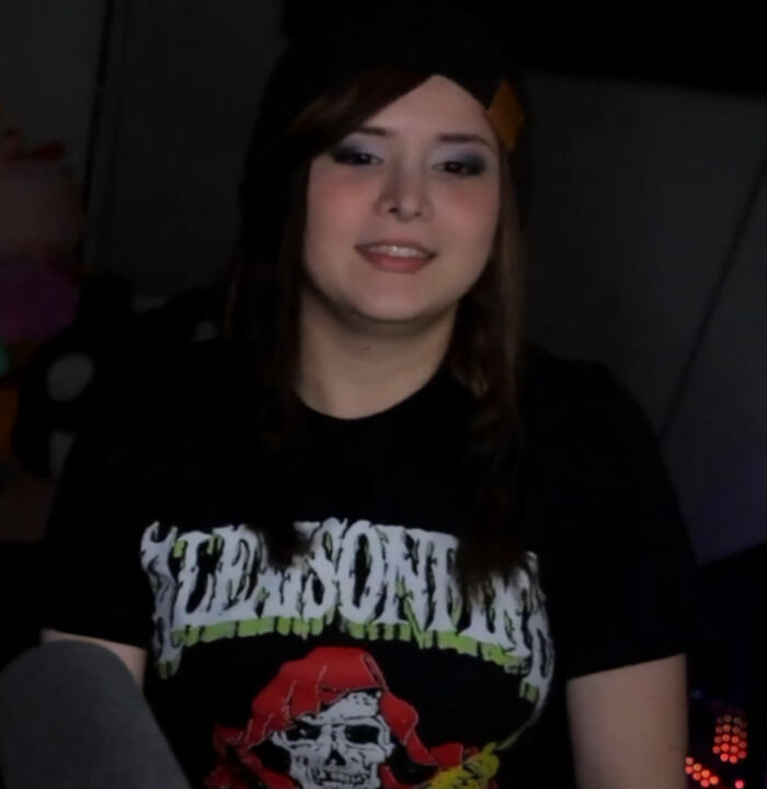 A Goth Baddie before her transformation, smiling at the camera, wearing a dark t-shirt. A Goth Baddie before her transformation, smiling at the camera, wearing a dark t-shirt.