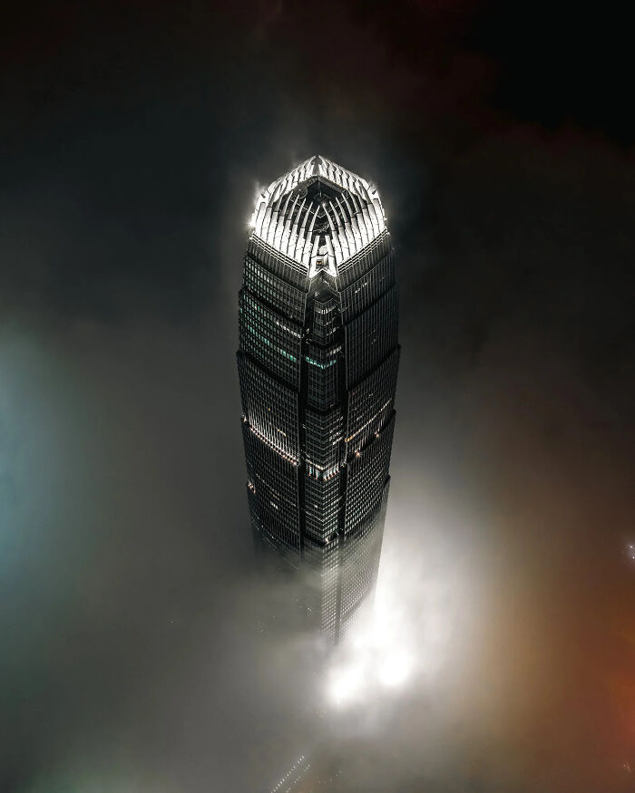 A towering skyscraper enveloped in mist, its top illuminated, a breathtaking image from the European Photography Awards.