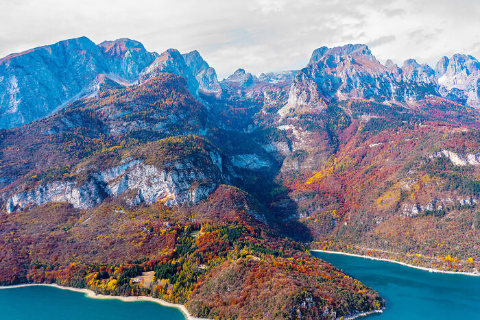 A breathtaking aerial view of mountainsides in autumn colors overlooking a serene lake, a stunning nature photography.