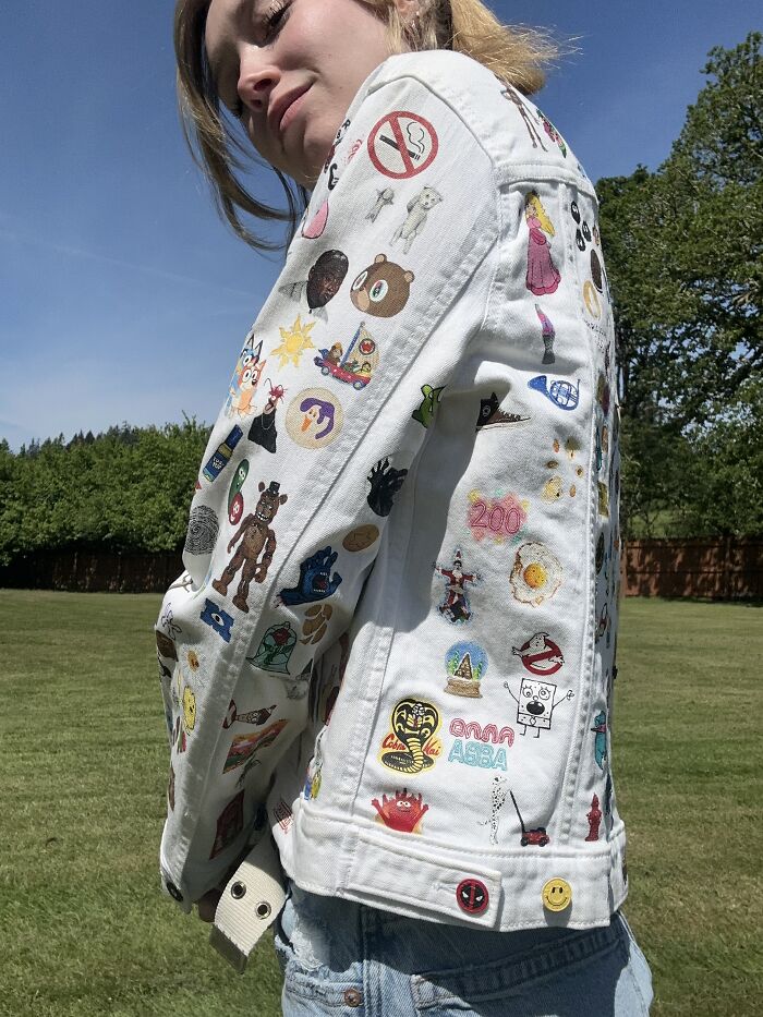 A person wearing a white denim jacket, adorned with colorful pop culture pins and patches, representing Gen-Z childhood.