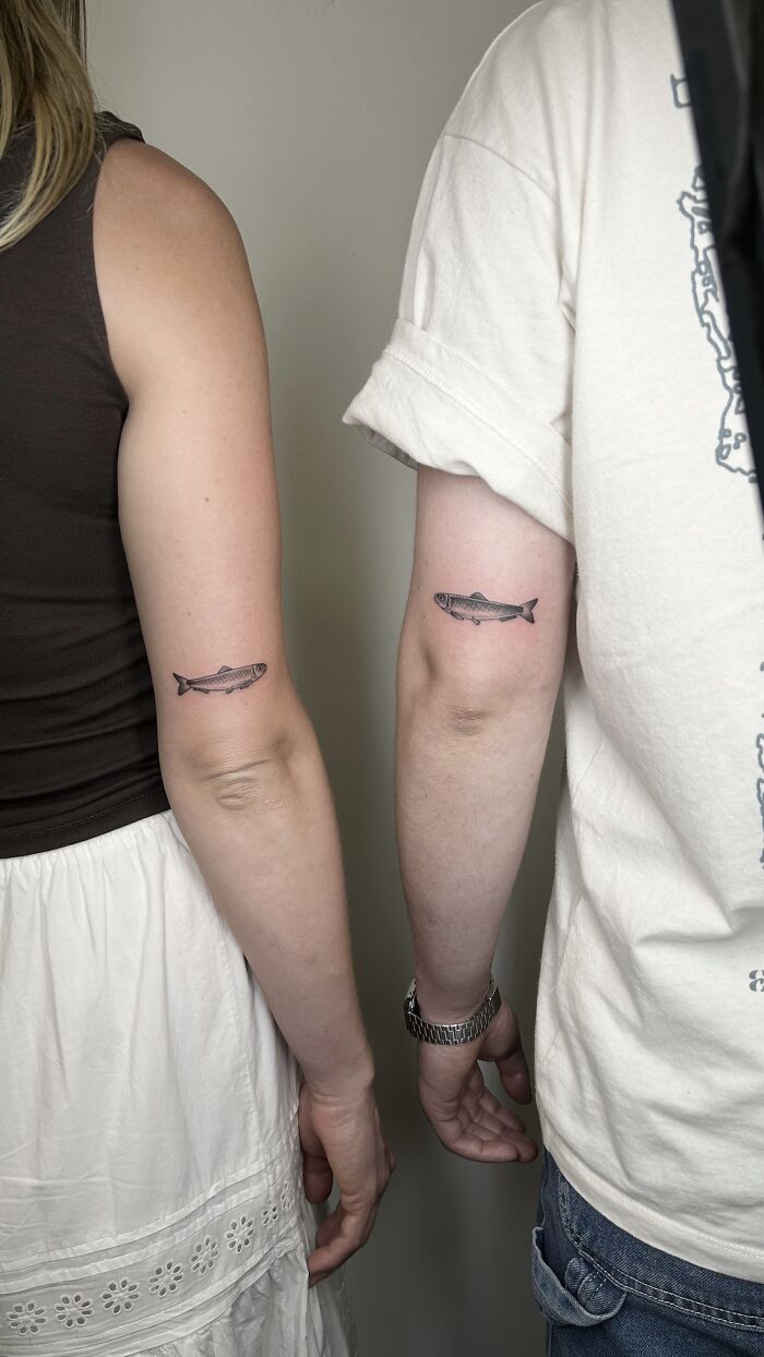 Matching ink ideas: two people showing off fish tattoos on their forearms.