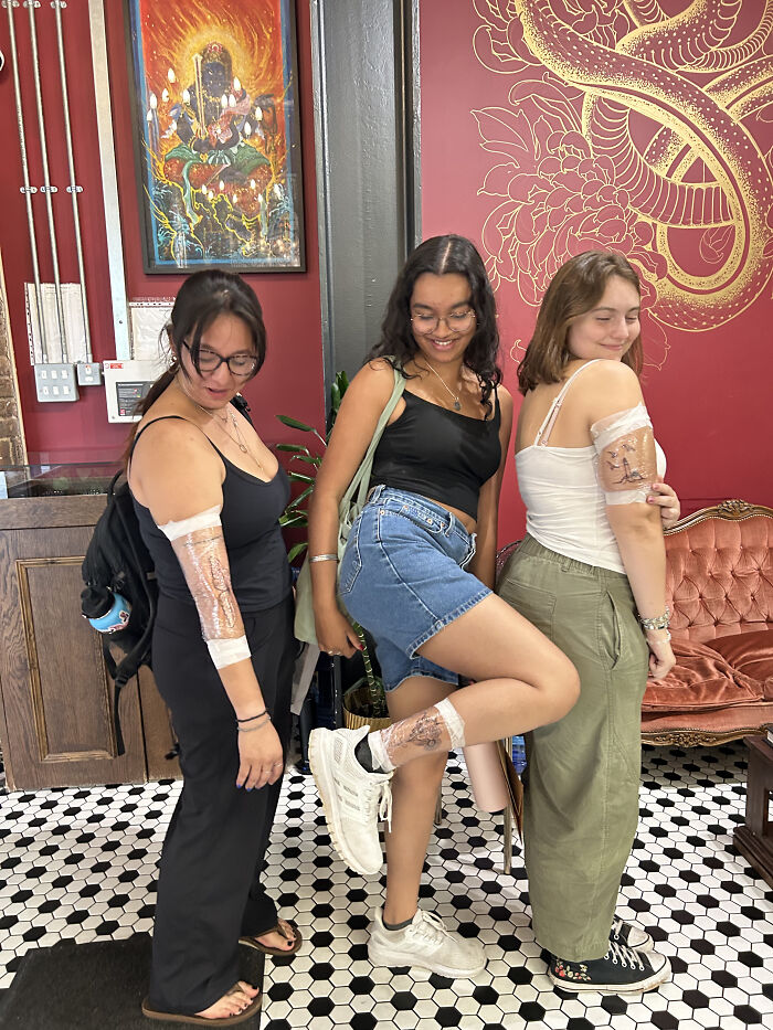Three friends show off their fresh matching ink ideas, bandaged on their arms and legs after getting tattoos.