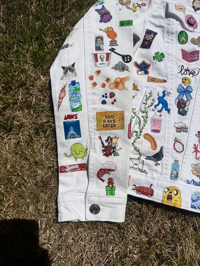 Close-up of the left sleeve of a white denim jacket, showcasing a collection of pop culture art from Gen-Z childhood.