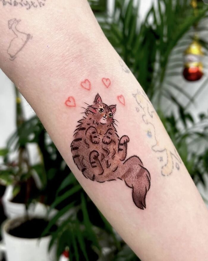 A sweet tattoo in the style of crayon drawings, featuring a fluffy brown cat surrounded by red hearts, highlighting artistic childhood creativity.