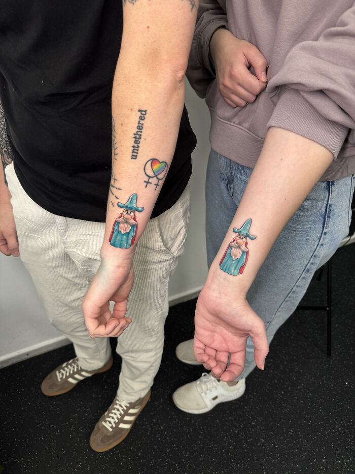 Two individuals showing off matching ink ideas of gnome tattoos on their forearms, with other tattoos visible above.